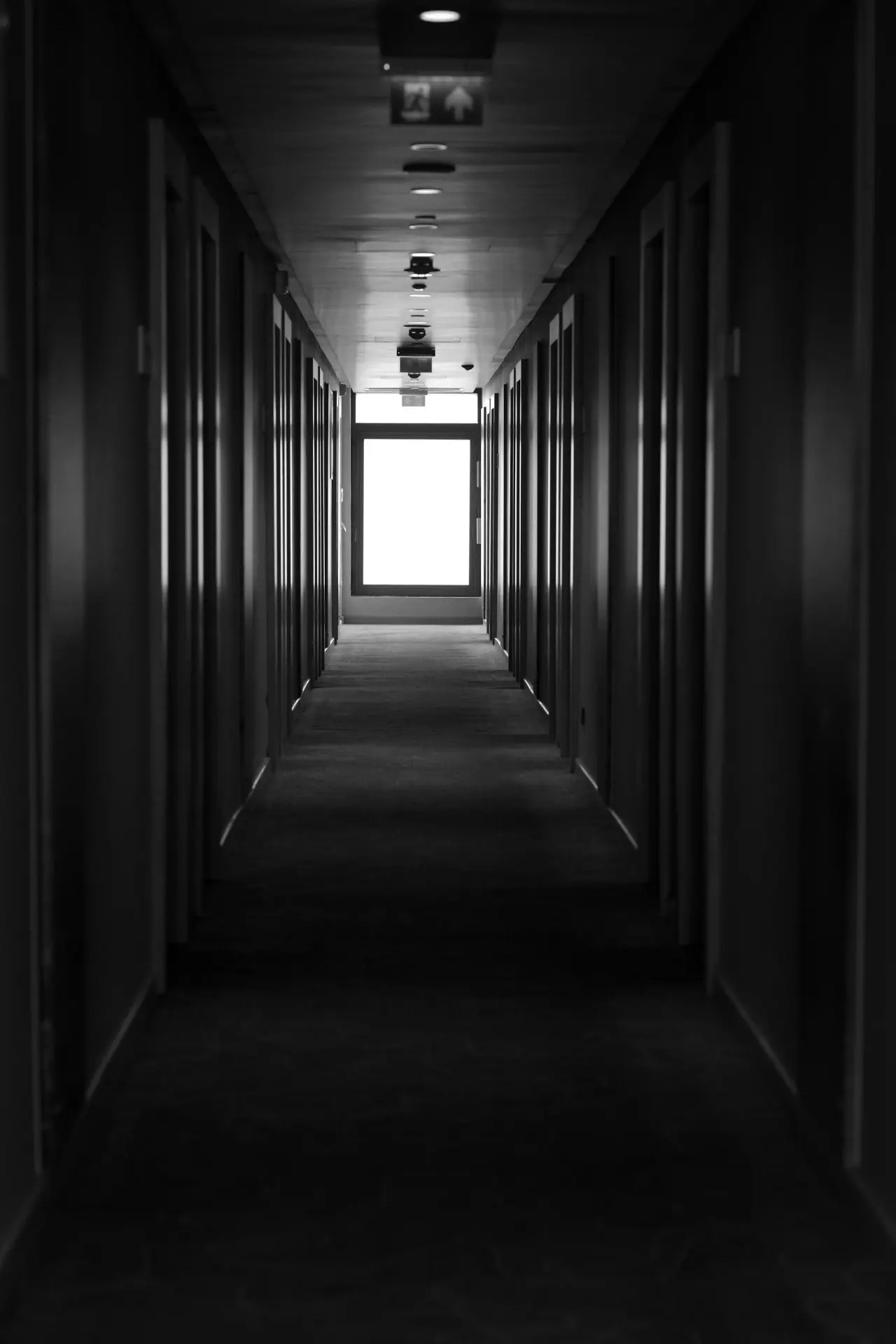 Dark monochrome corridor leading toward a bright exit, symbolizing disciplined transition from signal to decision logic.