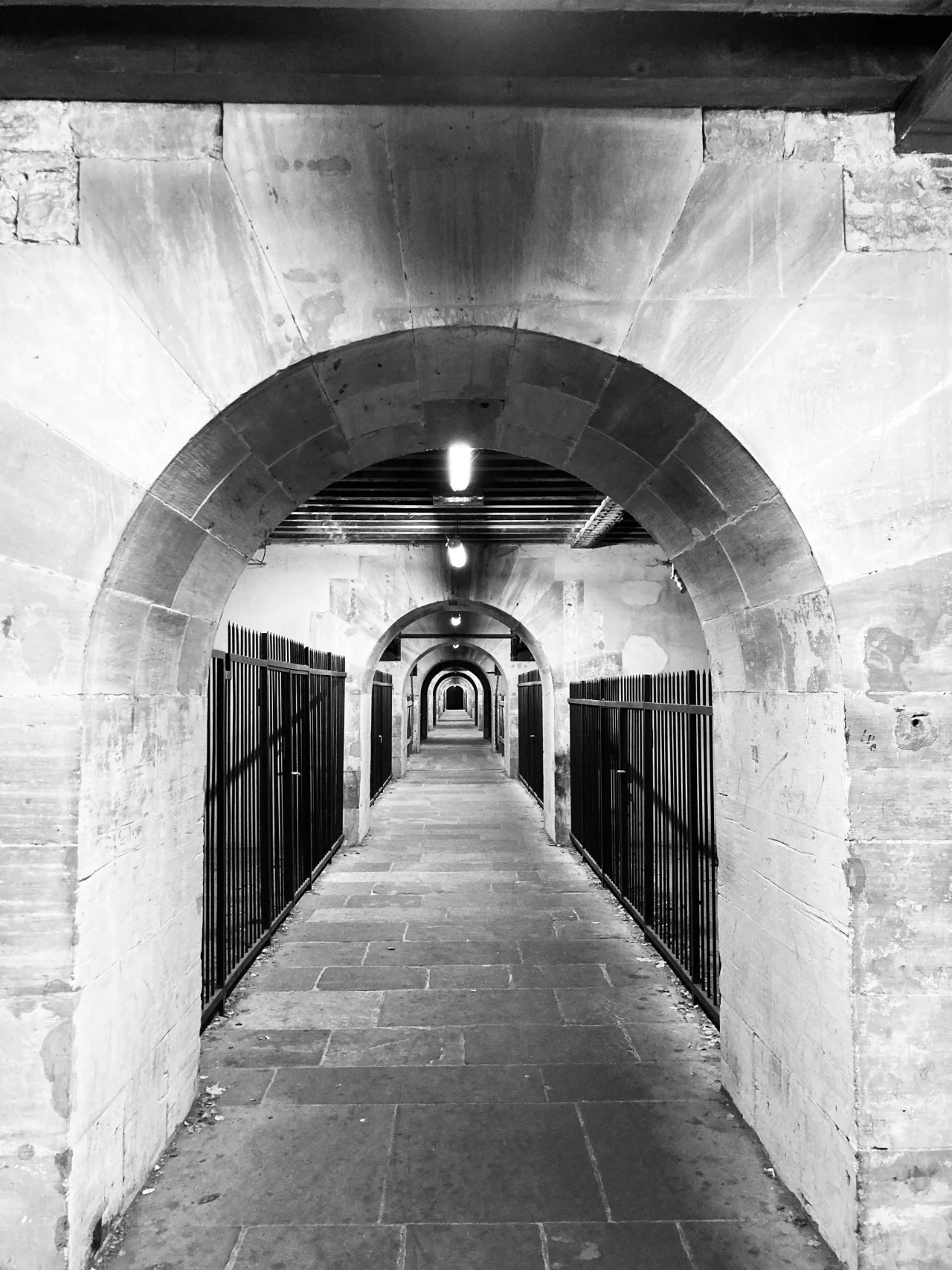 Black-and-white tunnel framed by repeating concrete arches, representing endurance through compression and controlled passage.