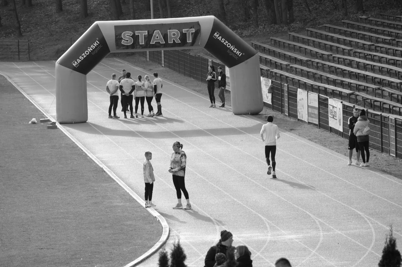 Monochrome running track with a start banner and athletes preparing, symbolizing threshold timing and endurance under pressure.